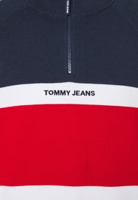 Pull rayé bleu marine, blanc et rouge avec une fermeture éclair à l'avant et "TOMMY JEANS" brodé sur la bande blanche.