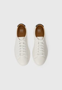 Hvide lædersneakers med en glat tekstur, rund tå, flade snørebånd og en brun sål med et logo. Sort akcent på hælen.