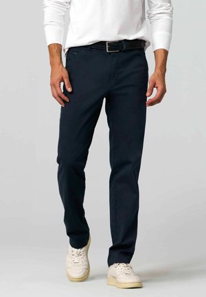 Marineblauwe chino broek van katoen, met een slim fit, zijzakken en een gevlochten zwarte riem. Gedragen met witte sneakers.