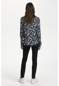 Mörkblommig blus med långa ärmar, med marinblå bakgrund och ljusa blommönster, kombinerad med svarta byxor och ljusa sneakers.