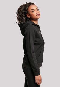 Black zip-up hoodie with a kangaroo pocket, textured fabric, and a hood. The design includes ribbed cuffs and a relaxed silhouette.