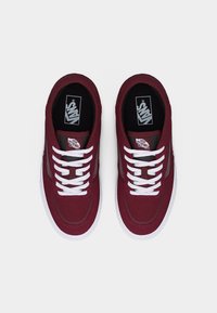 Ζευγάρι μπορντό αθλητικά παπούτσια Vans με λευκά κορδόνια και λευκές σόλες, σε θέα από πάνω σε απλό λευκό φόντο.