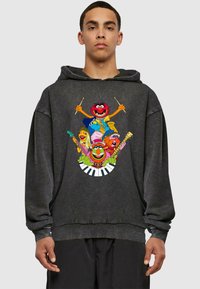 Sort oversized hoodie med et farverigt grafisk motiv af tegneseriefigurer, der spiller musikinstrumenter, sat mod en subtil slidtegn tekstur.