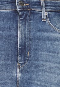 Denimjeans med en medelblå tvätt, som har dragkedja, knappstängning och subtila blekningar. Klassisk femfickdesign med synlig sömnad.