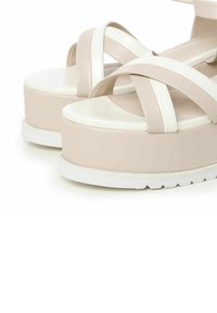 Sandalias de plataforma con diseño de tiras cruzadas en beige y blanco. Fabricadas en material sintético suave, cuentan con una suela de goma y una suela gruesa.