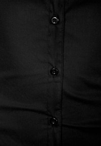 Gros plan sur le devant d'une chemise en tissu noir avec quatre boutons noirs visibles alignés verticalement au centre.
