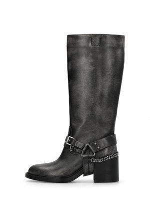 Botte noire en cuir mi-mollet avec un talon bloc, des sangles décoratives, des boucles métalliques et un détail chaîne autour de la cheville.
