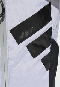 Acentos geométricos negros sobre una tela blanca texturizada con un patrón de diamantes; presenta una cremallera gris y un detalle de malla negra.