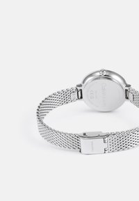 Bracelet de montre en maille argentée avec un fond de boîtier poli, doté d'un fermoir. Logo gravé "Calvin Klein" et design circulaire.