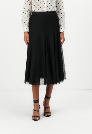 Jupe midi noire en tulle superposé avec une finition texturée, dotée d'une large taille élastique. Associée à des sandales à lanières noires.