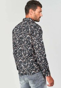 Camisa negra de botones con patrón floral blanco y acentos rojos, con mangas largas y dobladillo recto, hecha de tejido ligero.