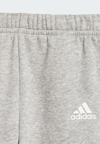 Pantaloni tuta grigi in cotone con vita elastica a coste, caratterizzati dal logo bianco adidas sul lato destro in basso. Texture morbida, design casual.