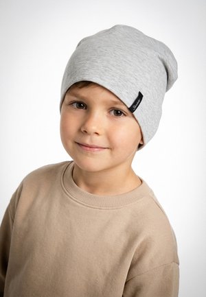 Young boy wearing a light gray beanie and beige sweatshirt, smiling softly against a plain white background.