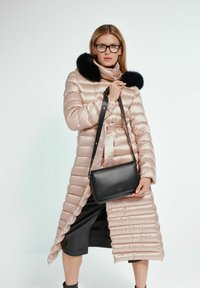 Jasnoróżowa kurtka puchowa z futrzanym kołnierzem, z zamkiem błyskawicznym i paskiem w talii; w połączeniu z czarną torebką na ramię.