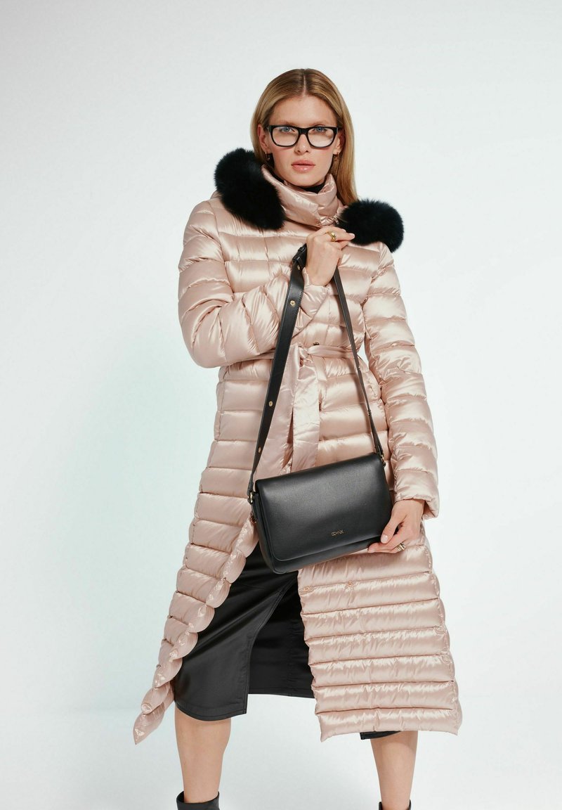 Jasnoróżowa kurtka puchowa z futrzanym kołnierzem, z zamkiem błyskawicznym i paskiem w talii; w połączeniu z czarną torebką na ramię.