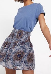 Sininen puuvillapaita yhdistettynä navynsiniseen ja kermanväriseen kuvioituun minihameeseen, jossa on kukka- ja geometrisia kuvioita sekä kerroshame.