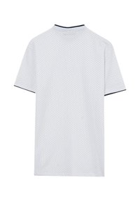Chemise blanche à manches courtes avec un petit motif de pois noirs, col plat et bordure navy le long de l'encolure et des manches.