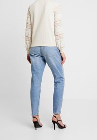 Světle béžová mikina s krajkovým lemem na rukávech, ve spojení se světle modrými džínami s rovnými nohavicemi a černými vysokými podpatky.