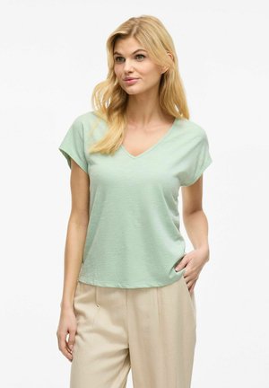 Light green short-sleeved top with a V-neck. Soft texture and relaxed fit. Paired with beige trousers for a casual look.