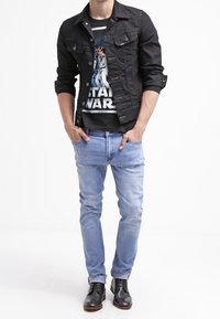 Chaqueta de denim negra con cierre de botones, camiseta gráfica de Star Wars, jeans slim-fit azul claro y zapatos de vestir negros. Look sencillo y casual.