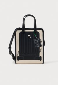 Bolsa retangular preta e bege com alças curtas, apresentando um padrão de bagagem e uma etiqueta. Feita de material resistente, com uma textura suave.