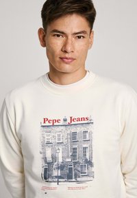 Bílá mikina s grafickým potiskem zobrazujícím vintage budovu, text "Pepe Jeans" v červené barvě a kulatý výstřih.