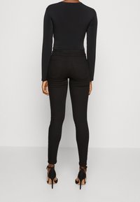 Svart bodysuit med långa ärmar i kombination med tighta svarta jeans. Högmidjad design med bakfickor, kompletterad av svarta högklackade skor.