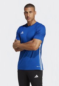 Sinine lühemate varrukatega sportlik särk, millel on kolm valget triipu külgedel. Valmistatud kergest materjalist, ümara kaelusega.