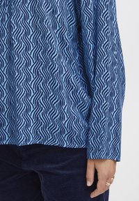 Blue patterned top featuring wavy, abstract lines in navy. Made of a soft fabric with a loose fit, paired with dark corduroy bottoms.