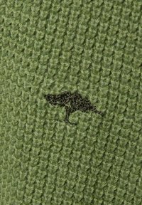 Grüner Strickstoff mit strukturiertem Muster und einem dunkelgrünen Baum-Logo, das in der Nähe des unteren Randes eingestickt ist.