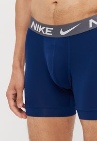 Mørkeblå Nike boxer briefs med grå elastik, der har hvidt logo, glat stof, tætsiddende design og sømdetaljer.
