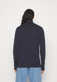 Maglione blu navy con colletto alto, maniche lunghe e polsini a costine. Realizzato in un materiale morbido, presenta una texture liscia e dettagli minimi.