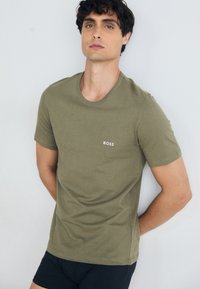 Olivgrünes T-Shirt mit kurzen Ärmeln und Rundhalsausschnitt, mit weißem "BOSS"-Logo auf der Brust, aus weicher Baumwollqualität.