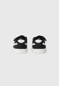 Baskets noir et blanc avec un dessus en tissu texturé, semelle en caoutchouc blanche et un détail de logo doré au niveau du talon. Dotées de bandes Velcro.