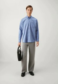 Light blue button-up shirt with a chest pocket, paired with gray wide-leg trousers and black shoes. Holds a black briefcase.