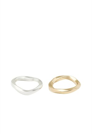Une bague en argent et une bague en or aux formes rondes, lisses et irrégulières sont placées côte à côte sur un fond blanc uni.
