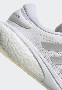 Witte sportschoen met een gemêleerde mesh bovenkant, gevoerde kraag en een gevoerde, gestreepte zool met een opvallend logo detail aan de zijkant.