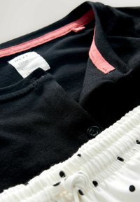Black top with pink inner collar and a white label partially visible, paired with white fabric featuring black polka dots and a drawstring.