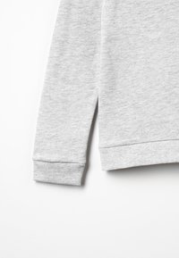 Manga de sudadera gris con puño acanalado y textura suave, con un patrón ligeramente jaspeado visible en la tela.