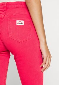 Högmidjade rosa denimjeans med en bakficka som har en vit Wrangler-logoetikett och distinkta sömnadsdetaljer.