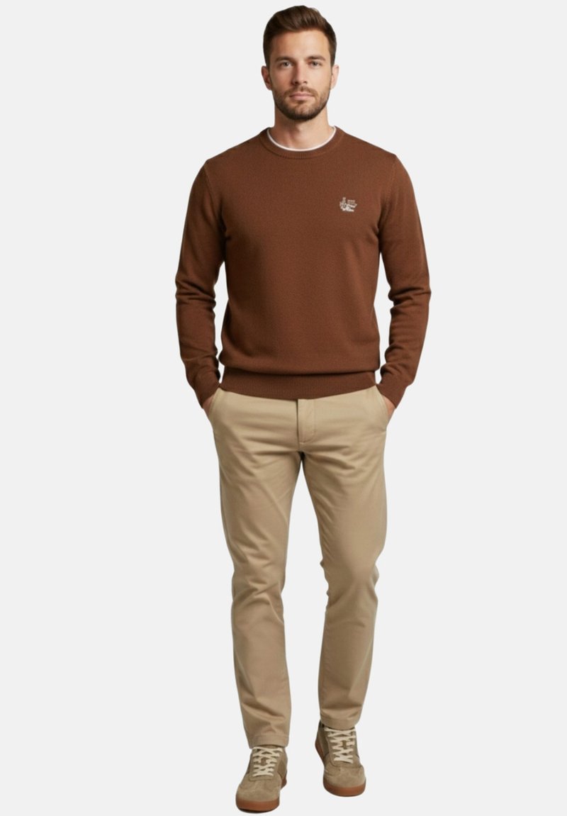 Sudadera marrón con textura y cuello redondo, combinada con pantalones beige claro y zapatillas beige. Detalle sutil del logo en el pecho.