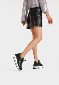 Sneaker in pelle nera con suola bianca e nera, punta rotonda, cuciture decorative e lacci. Abbinate a un top di paillettes argento e una gonna di pelle.