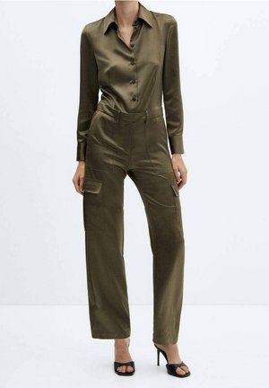 Olivenfarvet satin jumpsuit med design som en knap-op skjorte, lange ærmer, høj talje, brede bukser og cargo-lommer. Sorte hæle sandaler.