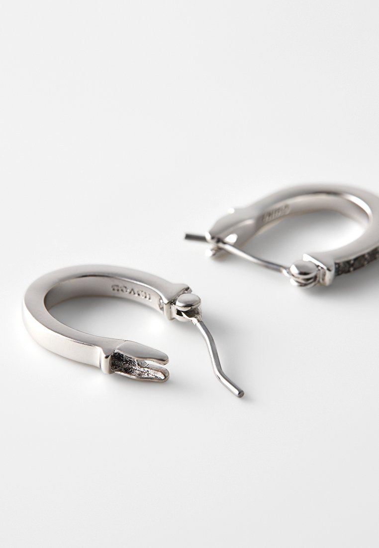 Silberne Creolen mit glatter Oberfläche, ausgestattet mit einem einzigartigen Verschluss und subtilen Texturakzenten nahe den Öffnungen.