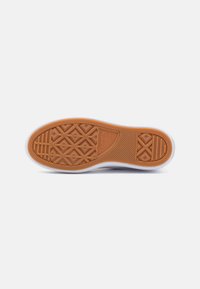 Biała podeszwa sneakersów z teksturowaną brązową gumową podeszwą z geometrycznymi wzorami, w tym szczegółami w kształcie diamentu i siatki.