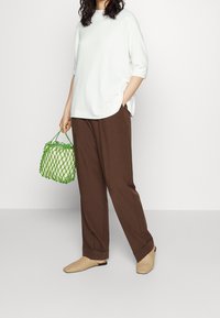 Biała bluzka z krótkim rękawem, brązowe spodnie o szerokich nogawkach, plecione beżowe buty wsuwane i zielona siatkowa torba, prezentowane na neutralnym tle.