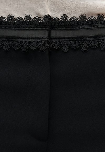 Μαύρο ύφασμα με διακοσμητική μαύρη δαντέλα και λεπτή λεπτομέρεια από σατέν κορδέλα κατά μήκος της άκρης σε μπεζ φόντο.