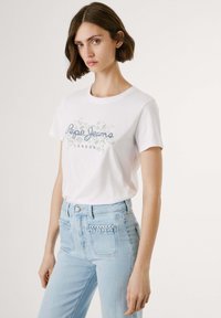 Vit bomull t-shirt med rund halsringning och tryckt design "Pepe Jeans London". Matchas med ljusblå hög midjejeans med vävda fickdetaljer.