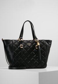 Black faux leather tote bag with a quilted design. Features gold hardware, dual handles, and a detachable strap with a tassel accent.