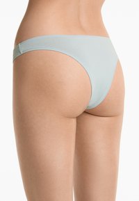 Een gedeelte van de onderrug en bovenbeen van een persoon is zichtbaar, gekleed in lichtblauwe bikinionderbroek, die de snit en pasvorm van het kledingstuk toont.